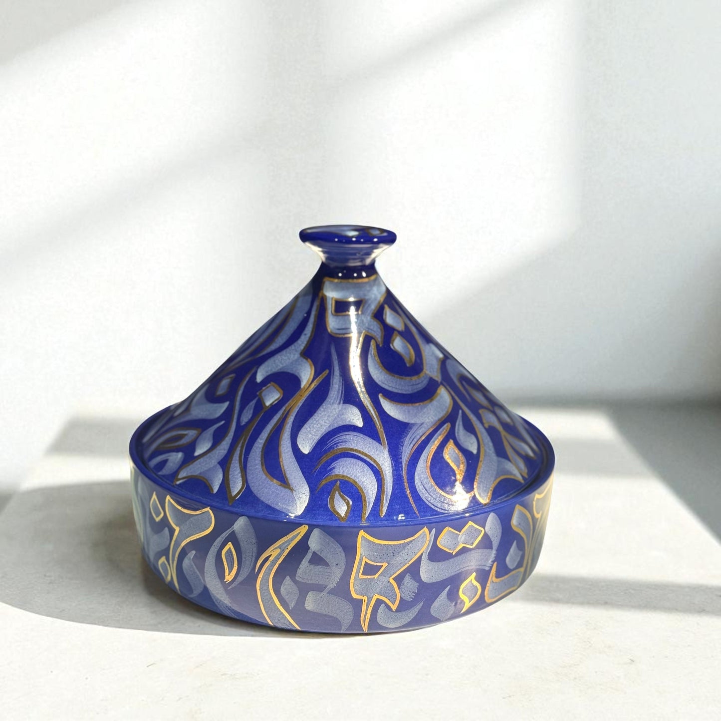 Decorative blue ceramic tagine with gold patterns on a white background